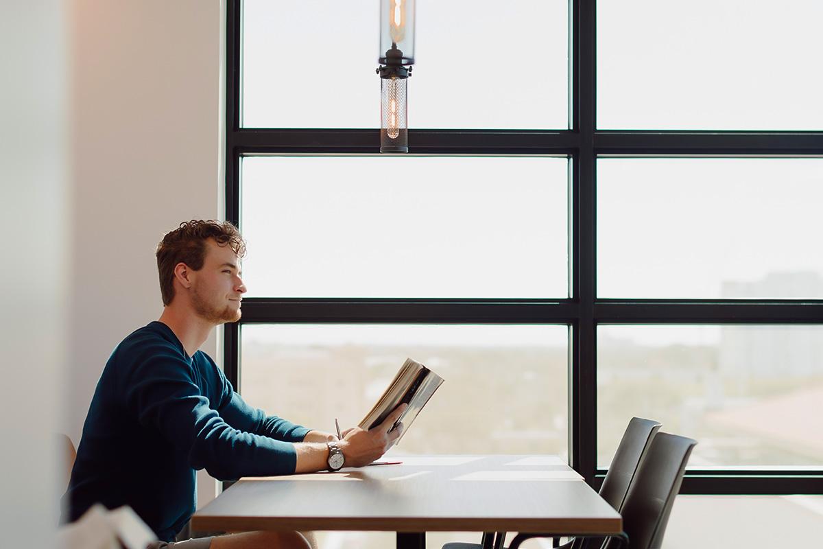 interdisciplinary studies student reads a book at a table near a window.